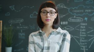 Young woman with glasses in front of chalkboard